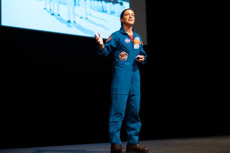 USNA female astronaut speaks on stage. 